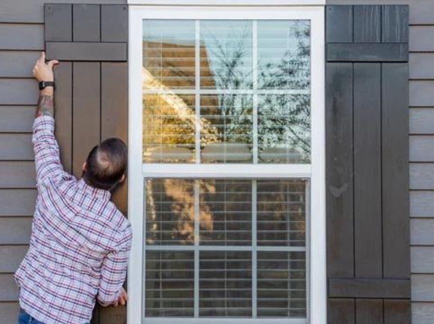 man installing a shutter on house